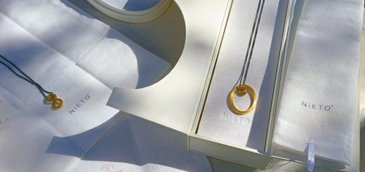 Gold circular pendant necklace displayed on white fabric with Nieto branding on boxes.