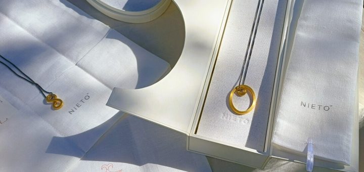 Gold circular pendant necklace displayed on white fabric with Nieto branding on boxes.