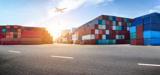 Port yard with colorful shipping containers, trucks, and an airplane taking off in a clear blue sky.