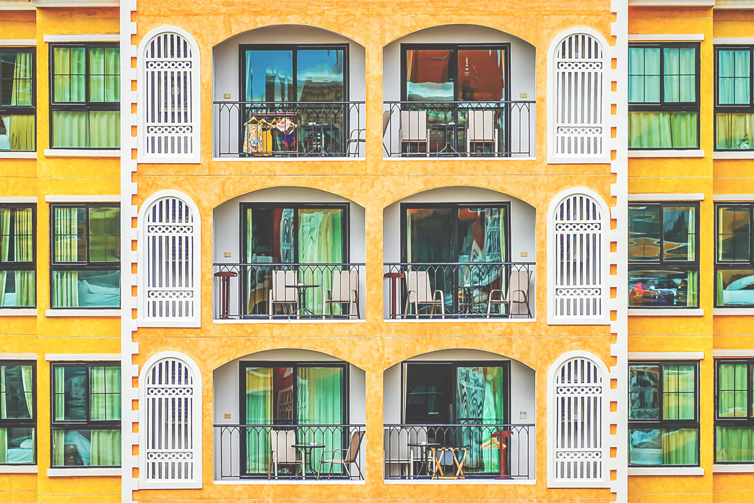 New vintage condo building blocks windows pattern - EconomiaeInversion.com Orange apartment building facade with three repeating balconies, arched openings, white decorative doors, and black railings.