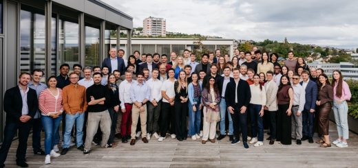 Large diverse group of professionals posing on a rooftop terrace with a city skyline in the background.