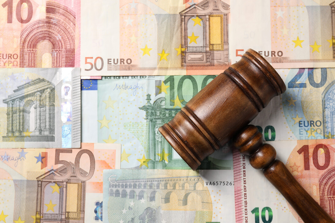 Wooden gavel rests on a collage of euro banknotes, symbolizing money and justice in legal matters.