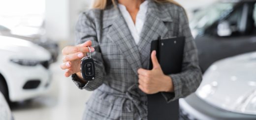 Woman in a checkered blazer handing over car key fob in a showroom, clipboard in hand