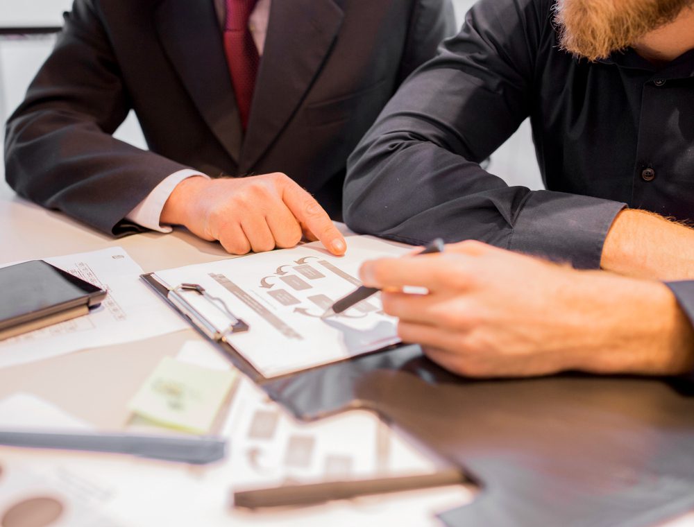 Two professionals review a document on a clipboard, one pointing with a pen at a chart.