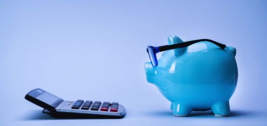 Blue piggy bank wearing glasses beside a calculator and smartphone, representing budgeting and savings.