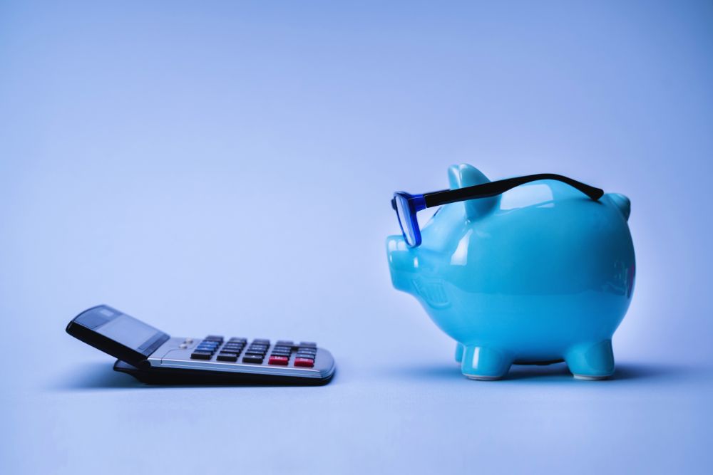 Blue piggy bank wearing glasses beside a calculator and smartphone, representing budgeting and savings.