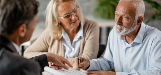 Older couple signs a document with a professional at a table during a meeting.