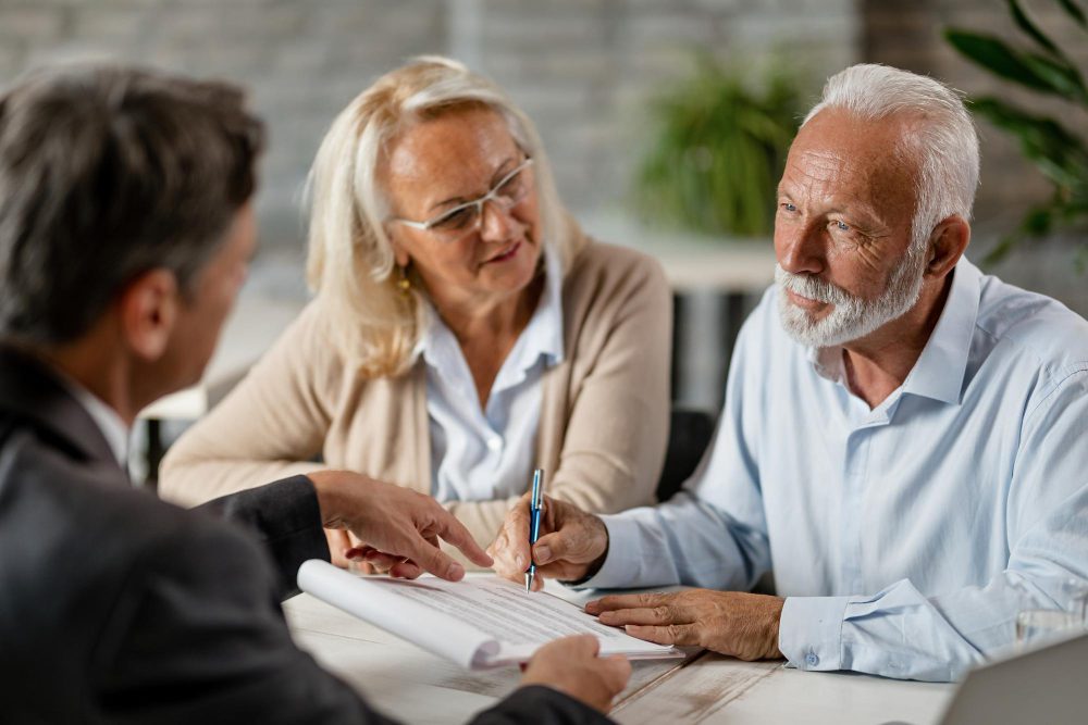 Older couple signs a document with a professional at a table during a meeting.