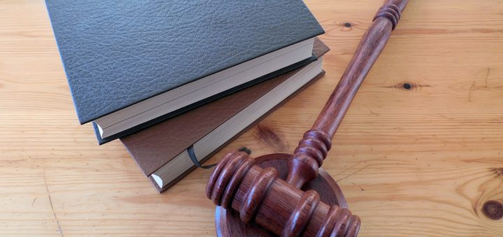 Gavel resting on a stack of three hardbound books on a wooden table, symbolizing law and justice.