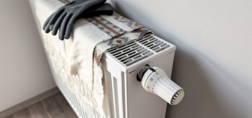 White radiator with a large thermostat knob, a plaid blanket draped over it, and a pair of gray gloves resting on top.