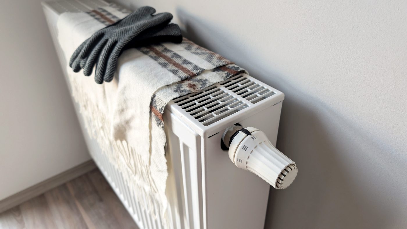 783996 J Abad Codelco - EconomiaeInversion.com White radiator with a large thermostat knob, a plaid blanket draped over it, and a pair of gray gloves resting on top.